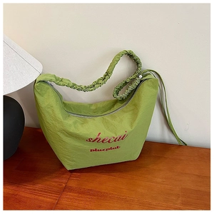 Detail of green crescent bag featuring ruched strap and silver zipper on wooden desk