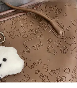 Dettaglio borsa in pelle marrone con icone sbalzate e ciondolo di peluche bianco