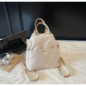 Détail du sac en nylon crème imperméable avec bandoulière colorée sur un lit blanc