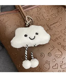 Dettaglio di un ciondolo a nuvola in peluche con ricamo e pompon su una borsa