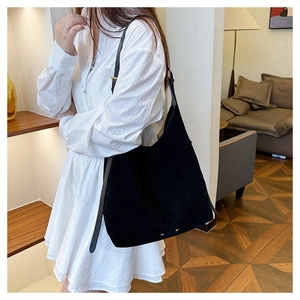 Detail of black matte suede tote bag with gold hardware rivets on a white dress model