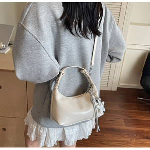 Détail d'un sac demi-lune blanc crème brillant avec un gland en forme d'étoile argentée