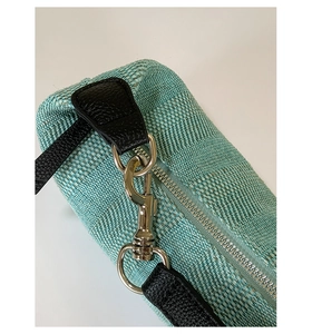 Close-up of mint green woven fabric texture with black leather strap and silver metal hooks