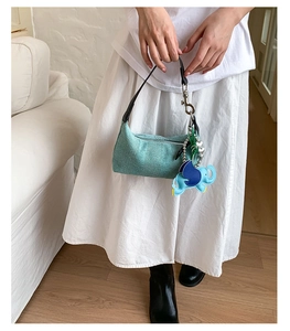 Detail of light green woven pillow bag with a blue elephant leather charm and silver zipper