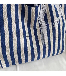 Détail du cabas en toile rayée bleue avec texte Melody rose et bordure en dentelle