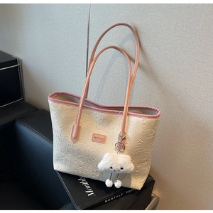 Dettaglio borsa tote color crema con bordi rosa, motivi a rilievo e ciondolo a nuvola