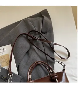 Detail of dark brown glossy leather crossbody bag with adjustable strap and knotted handle