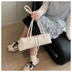 Close-up of white woven leather baguette bag with dual handles held by model