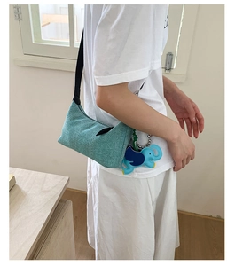 Close-up of a light green woven shoulder bag with a blue elephant charm on a model