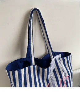 Détail du cabas en toile à rayures bleues avec nœud en dentelle et longues bandoulières