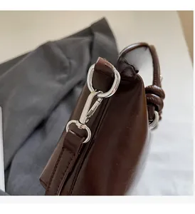 Close-up of glossy dark coffee faux leather with silver metal hook and knotted strap detail