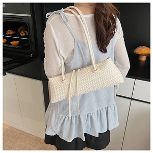 Minimalist white woven shoulder bag with long tassels shown in a cafe setting