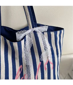 Détail d'un cabas en toile à rayures bleues avec lettrage rose et nœud en dentelle blanche