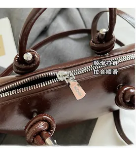 Detail of dark brown leather handbag with silver zipper and knotted handle design