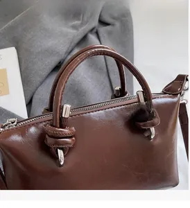 Detailed close-up of dark brown glossy pillow bag with unique knotted handle and silver hardware