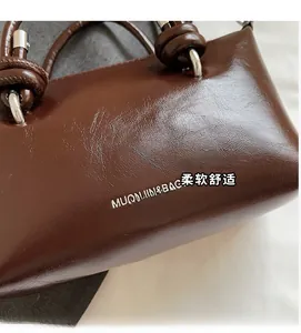 Detailed close-up of dark brown leather texture and knotted handle of the handbag