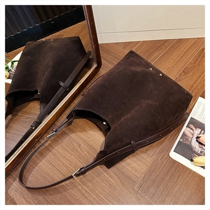 Close-up of brown suede tote bag with golden rivets on a mirror-reflected wooden floor