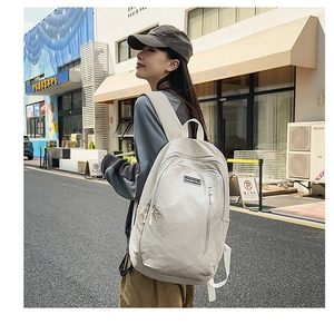 Outdoor street view of a woman wearing a cream canvas backpack with multiple zippers