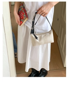 Detail of woven beige shoulder bag with black leather strap and silver metal hardware