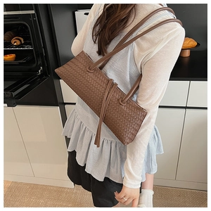 Close-up of brown woven leather baguette bag with dual straps and tassel zippers