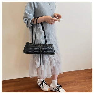 Detailed view of black woven leather underarm bag on a model with minimalist grey outfit