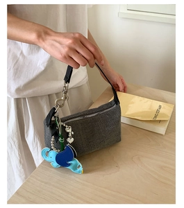 Detail of grey knitted shoulder bag with a blue elephant charm and black leather strap