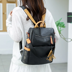 Detailed view of black patchwork backpack with brown leather tassel and stylish zippers