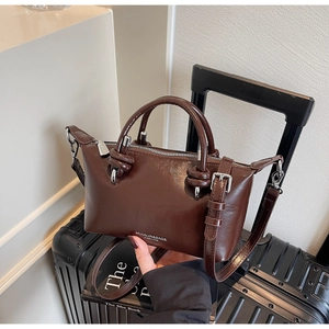 Detailed macro view of a glossy dark brown leather pillow bag with double handles and metal hardware