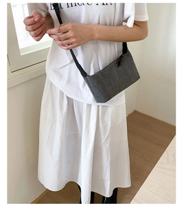 Detail shot of a grey woven textured crossbody bag paired with a minimalist white outfit