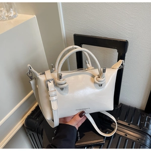 Detail of a creamy white crossbody bag with knot decor and silver hardware on a suitcase