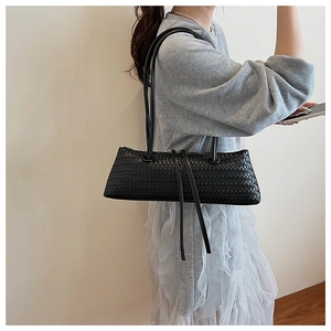 Close-up of black woven leather texture and shoulder strap on minimalist baguette bag