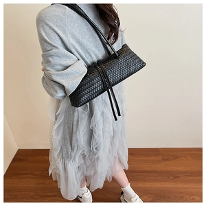 Detail view of the black woven leather texture and long tassel on a baguette bag