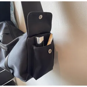 Dettaglio di una tasca laterale funzionale con bottone automatico su borsa a tracolla nera