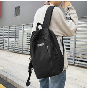 Outdoor shot of a minimalist black canvas backpack worn by a model against a modern wall
