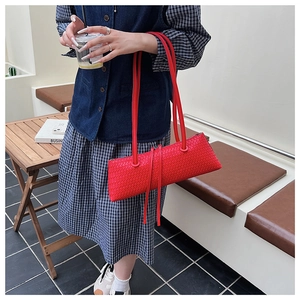 Close-up of a vibrant red woven underarm bag with leather tassels and dual straps