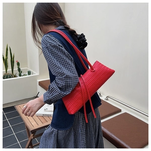 Detail of red woven leather underarm bag with long straps worn by a model in a stylish setting