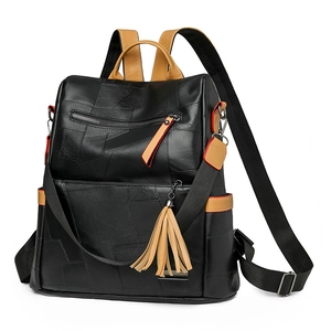 Detail of a minimalist black leather backpack with brown top handles and decorative tassel