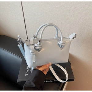 Detail of light blue faux leather handbag with knotted handles and adjustable strap