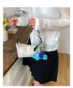 Detail of woven beige handbag featuring a vibrant blue elephant charm and black handles