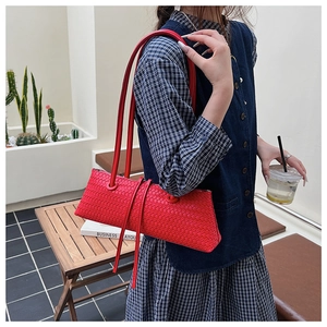Outdoor lifestyle shot of a red woven leather underarm bag with sleek shoulder straps
