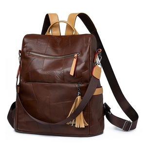 Detail view of brown patchwork leather backpack featuring zipper pockets and fringe tassel
