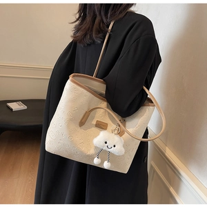 Dettaglio borsa shopper crema con motivi a rilievo e ciondolo nuvola su cappotto