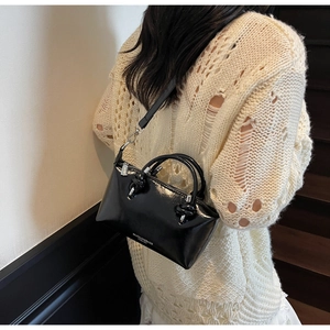 Glossy black patent leather bag with a knotted handle shown on model in a modern space