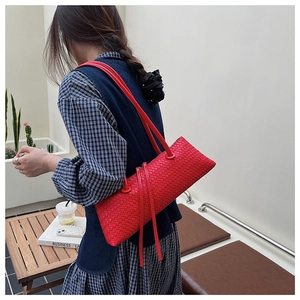 Lifestyle shot of a red woven baguette shoulder bag worn by a model in an outdoor cafe