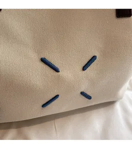 Detailed close-up of white canvas tote fabric with iconic blue four-corner stitch detail