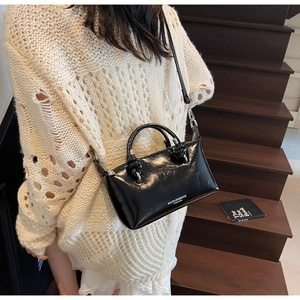 Detail of a black patent leather handbag featuring shiny texture and dual top handles