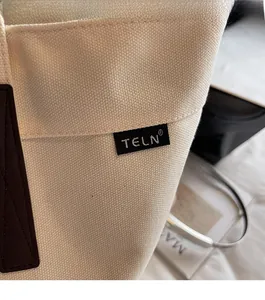 Detail of high-density cream canvas tote bag showing contrast leather trim and logo stitching