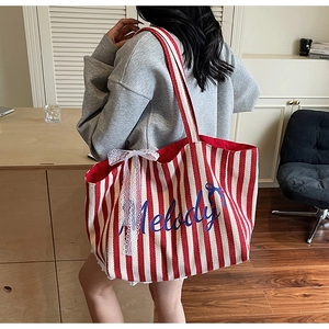 Détail d'un cabas en toile rayé rouge avec texte Melody et nœud en dentelle porté