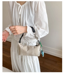 Minimalist beige woven handbag with black leather handles and blue dolphin charm detail
