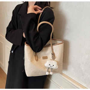 Dettaglio della borsa beige con motivi a rilievo e ciondolo a nuvola di peluche